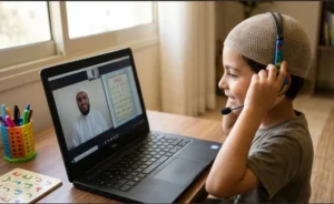 A young boy in a kufi sitting at a desk with a laptop, smiling while taking a trial lesson for online Quran classes for kids.